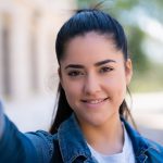 Portrait of young woman taking selfies while standing outdoors on the street. Urban concept.